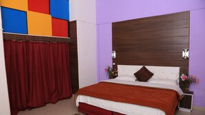 A bedroom with a large bed, a wooden headboard, a red curtain, and a wall with a colorful panel. - Prince Hotel (Dehradun)