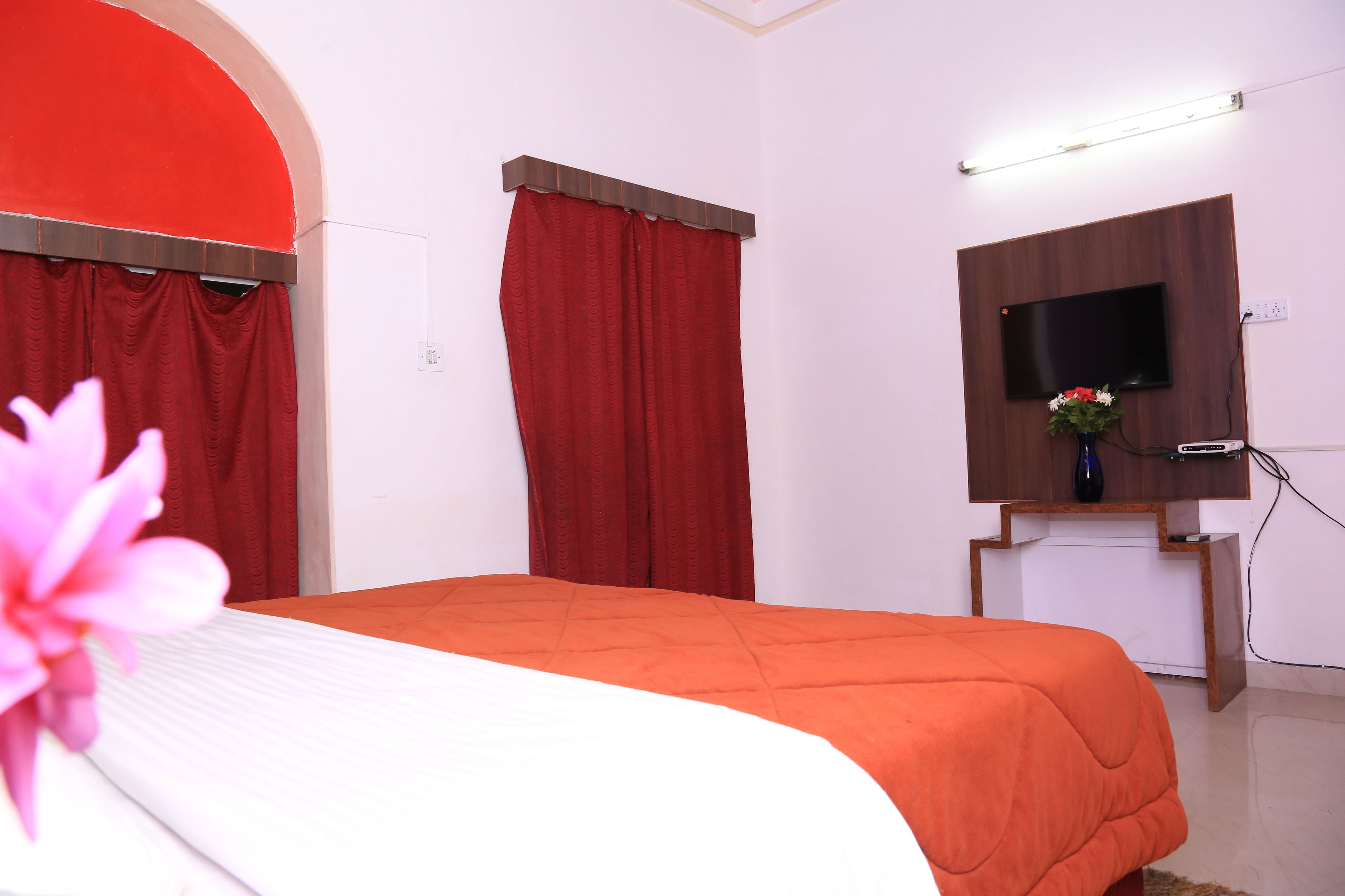 Una habitación de hotel con una cama, cortinas rojas, un televisor y un jarrón.