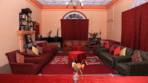 A living room with red sofas, a red carpet, and a chandelier. - Prince Hotel (Dehradun)