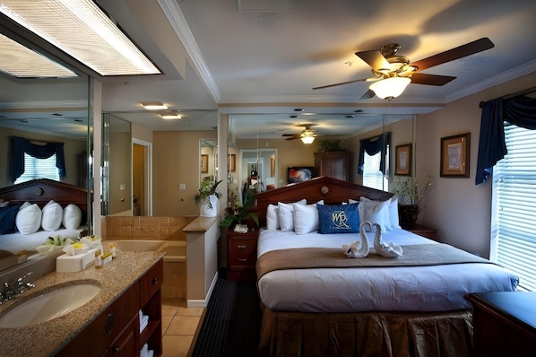 A hotel room with a large bed, a ceiling fan, a bathroom with a sink and mirror, and a view of the hallway. - Westgate Palace (Orlando)