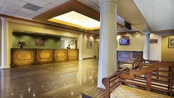 Um hall amplo com balcão de recepção, um banco de madeira e uma tela de televisão.