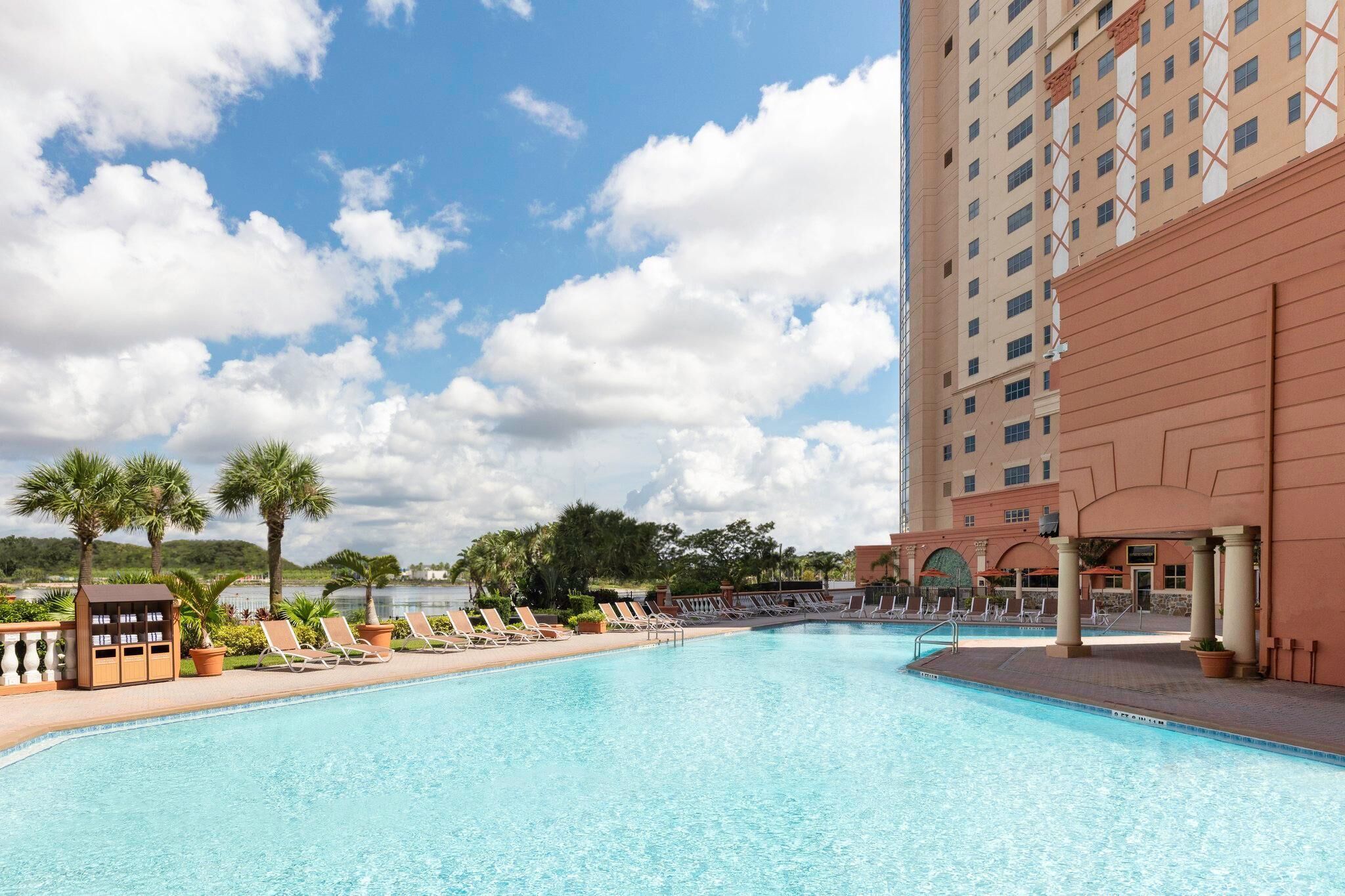 A swimming pool with lounge chairs, a building with columns, and a clear sky.