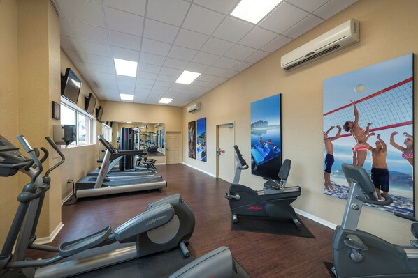 Una palestra con tapis roulant, ellittiche e una televisione a parete.