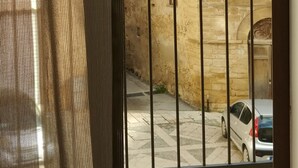A view through a window with a metal gate, a stone building, and a parked car. - B&B Il Campanile (Sciacca)