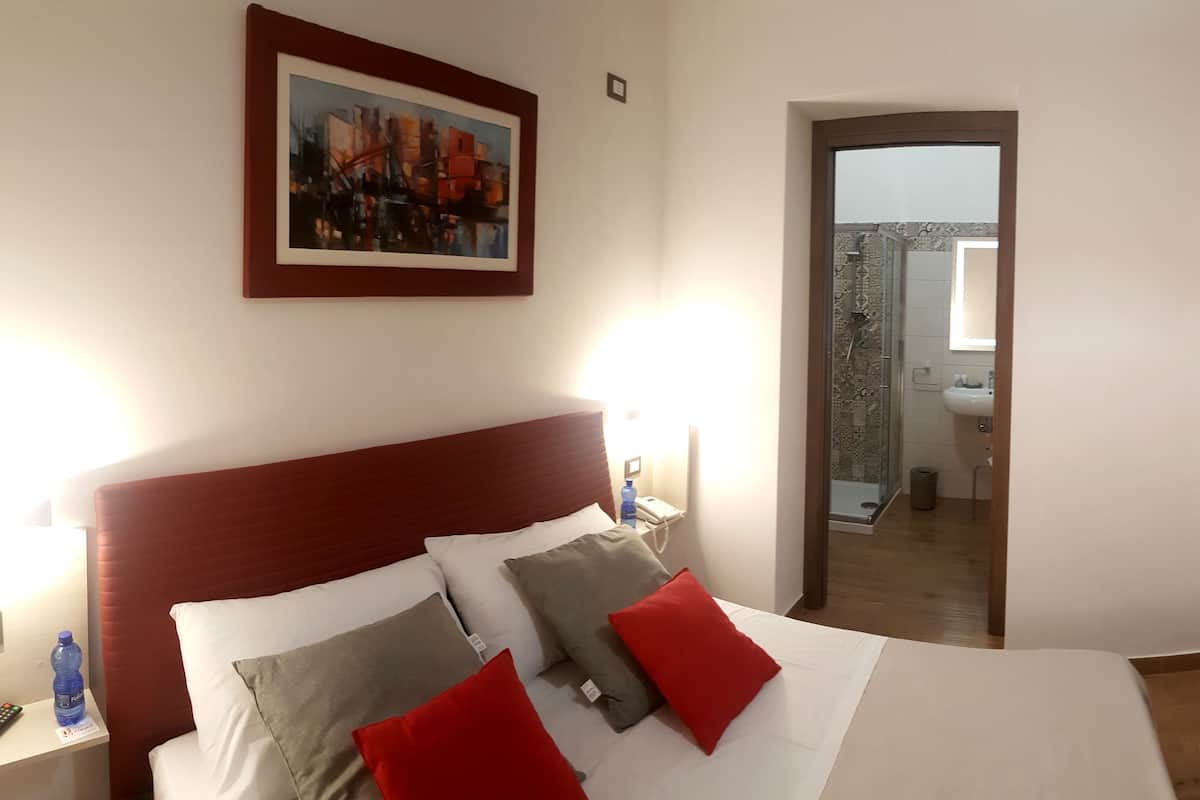 Une chambre d’hôtel avec un lit, un bureau, une armoire, un tableau et une salle de bain visible à travers une porte ouverte.