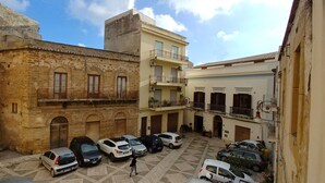 A courtyard with parked cars, a person walking, and buildings with balconies and windows. - B&B Il Campanile (Sciacca)