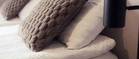 Una cama con ropa de cama blanca y dos almohadas con textura.
