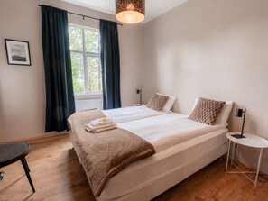 A bedroom with a large bed, a bedside table, a chair, a window with curtains, and a hanging light fixture. - Bjork Guesthouse (Bláskógabyggd)