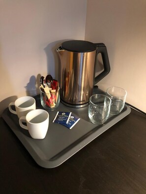 A tray with a stainless steel coffee pot, four white mugs, two glasses of water, and two packets of Melrose's Earl Grey tea.