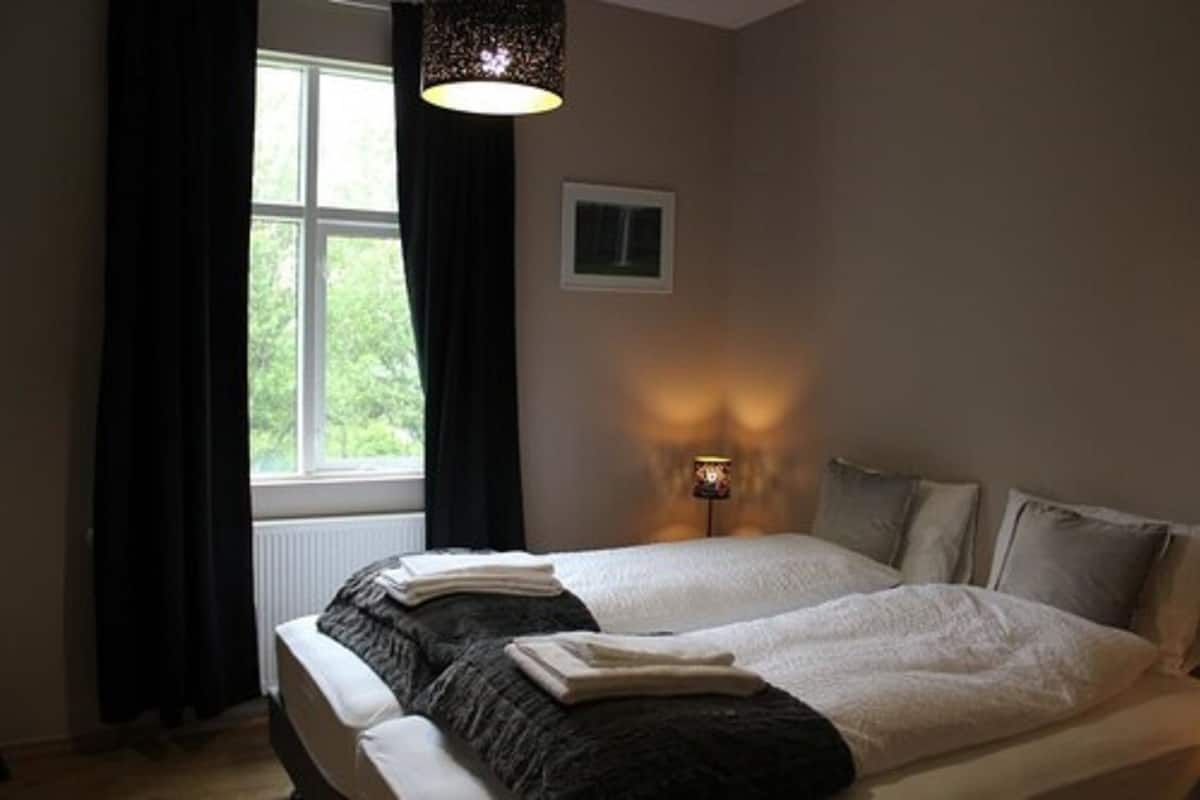 Un dormitorio con una cama grande, una ventana con cortinas, una lámpara de noche y un cuadro en la pared.