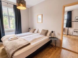 Un dormitorio con cama, mesitas de noche, un espejo y vistas al exterior.