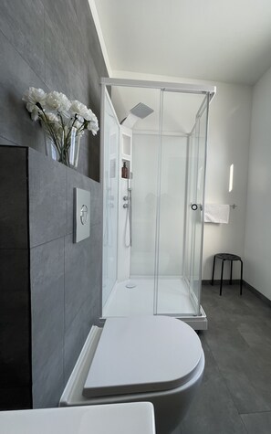 A modern bathroom with a glass-enclosed shower, a white sink, and a small stool.