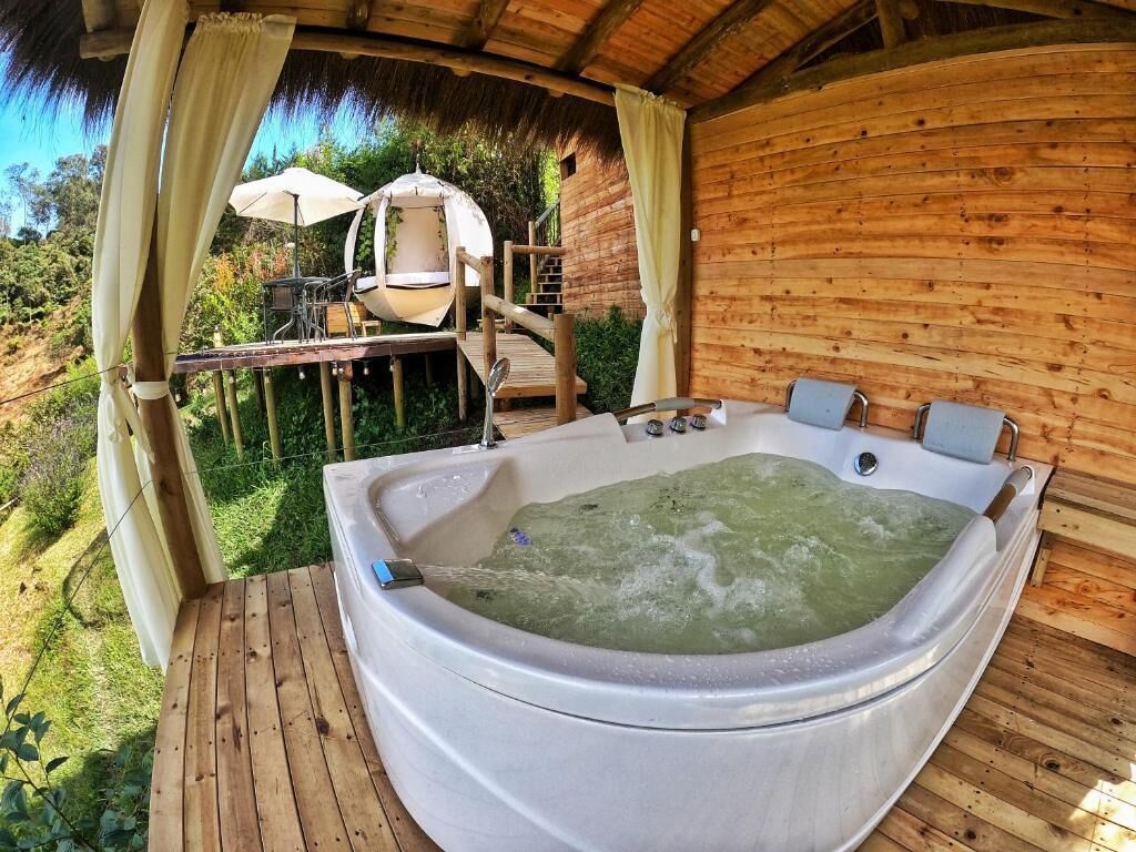Una cabaña de madera con jacuzzi, mobiliario exterior y techo de paja.