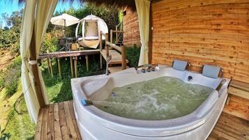 Una cabaña de madera con jacuzzi, mobiliario exterior y techo de paja.