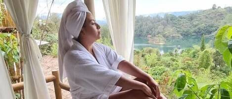 A person relaxing in a bathtub with a scenic view of a lake and hills.