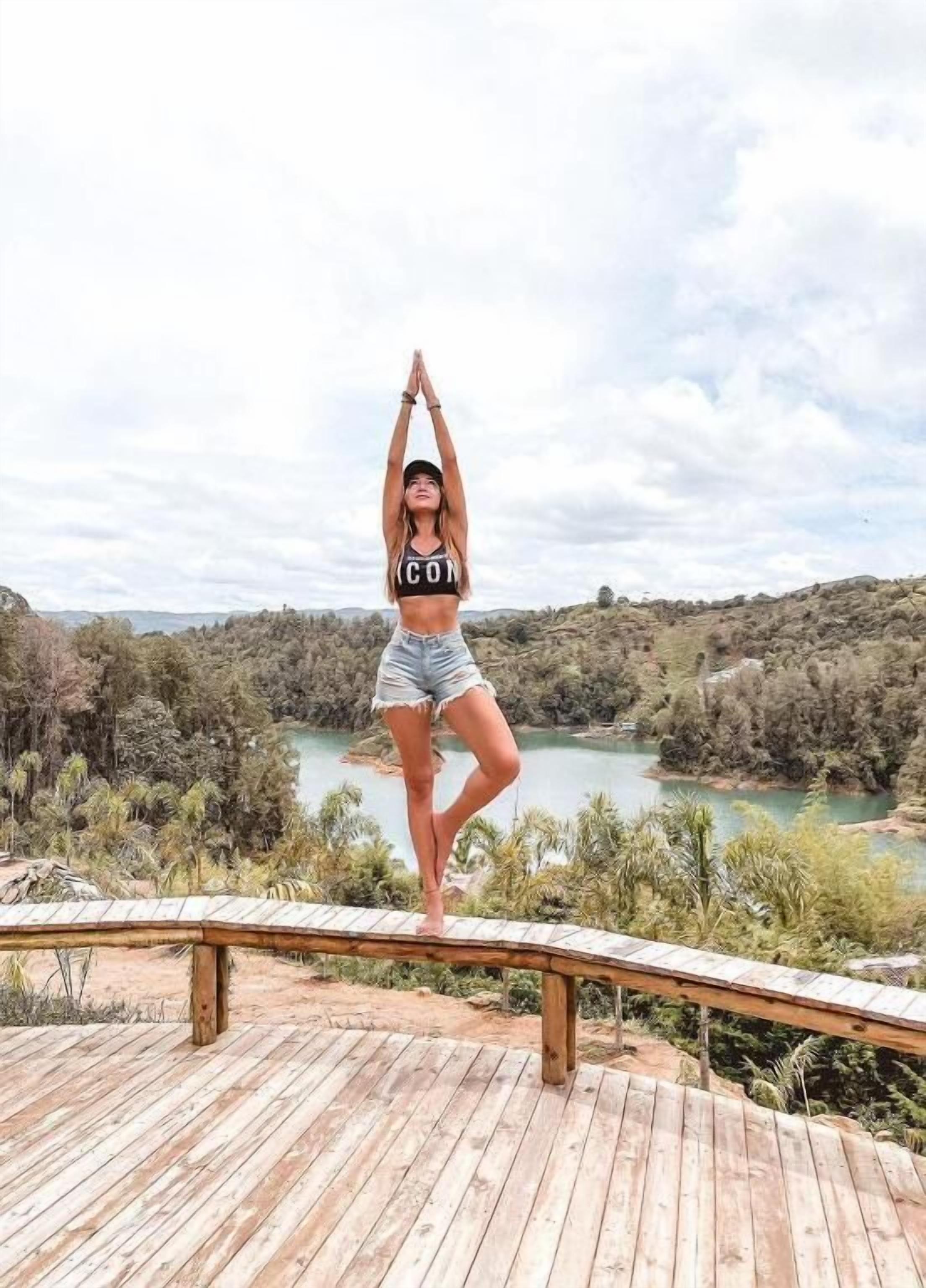 A person performing a yoga pose on a wooden deck with a view of a lake and hills in the background.