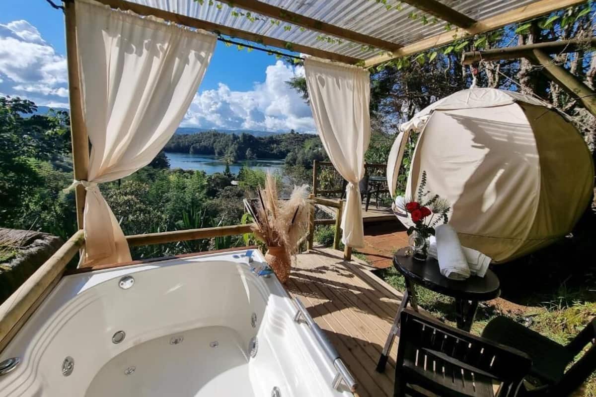 Uma banheira de hidromassagem sob uma pérgula, com vista para um lago e uma floresta.
