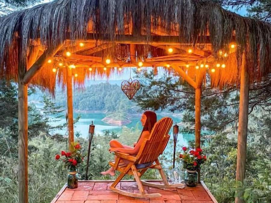 A wooden gazebo with a thatched roof, string lights, and a view of a lake.