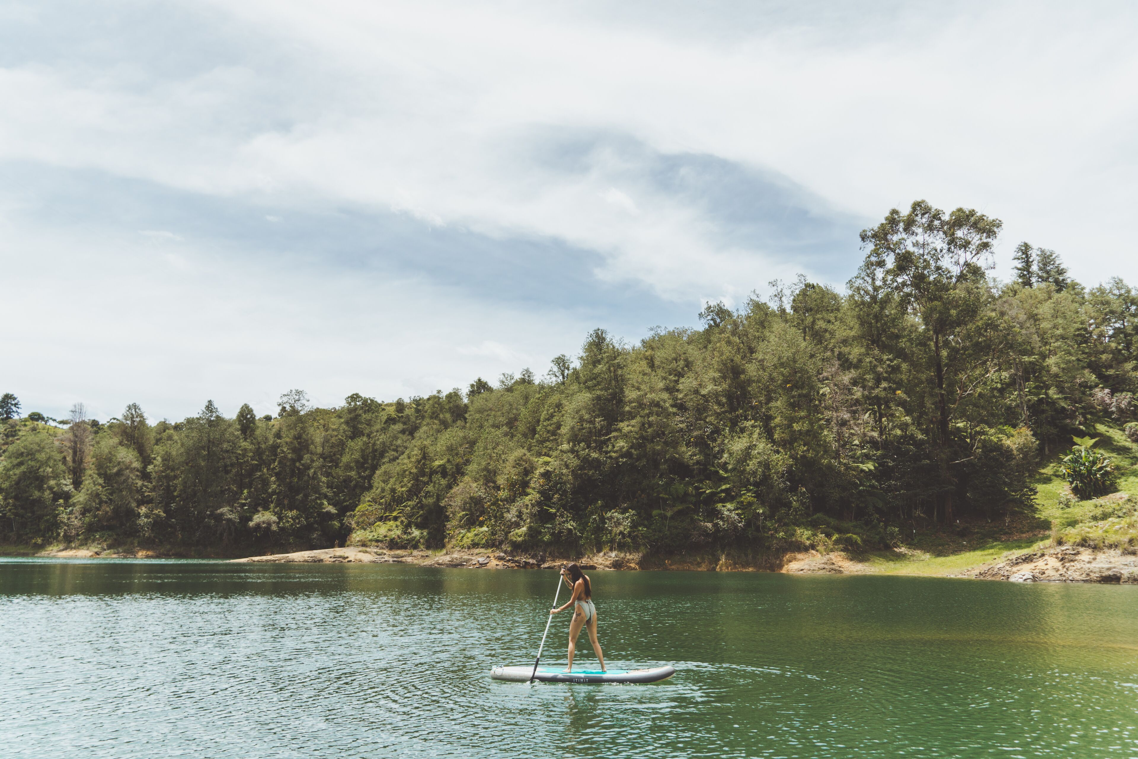 A person paddleboarding on a calm lake with a forested shoreline.