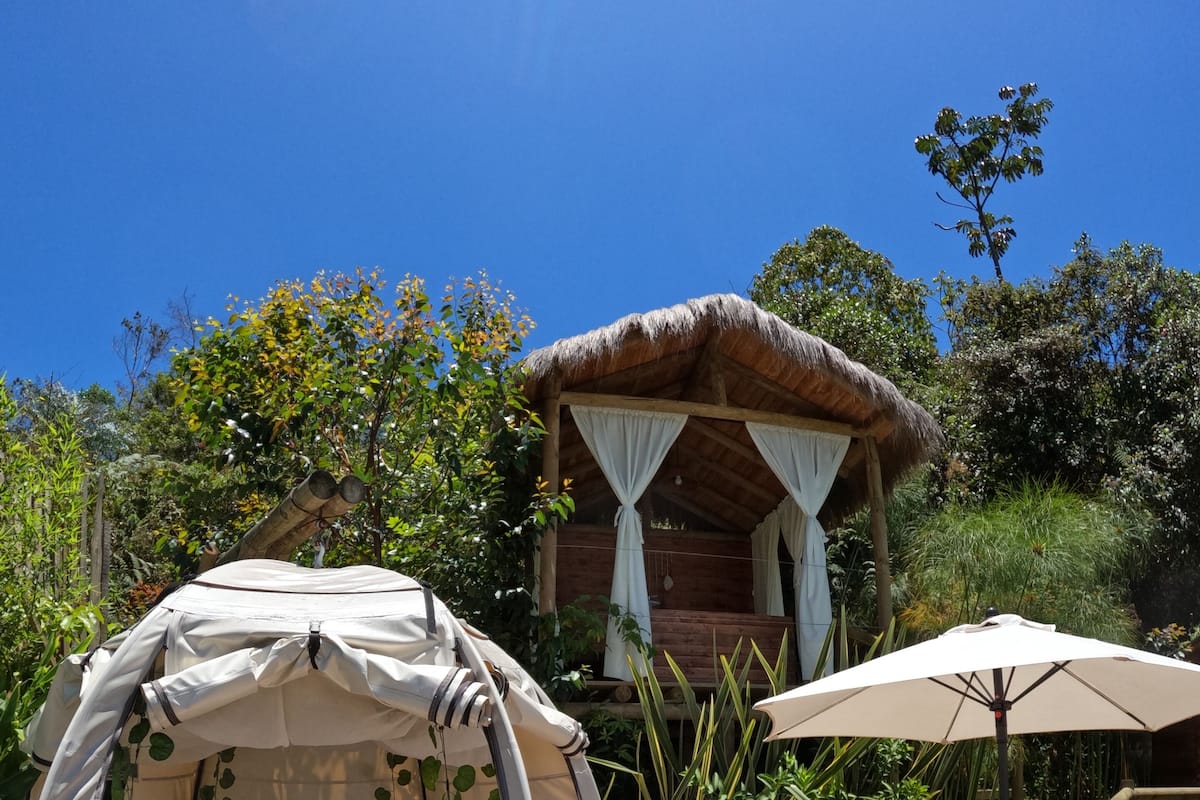 Uma cabana acolhedora ao ar livre, com cama, cercada por vegetação exuberante e um deck de madeira.