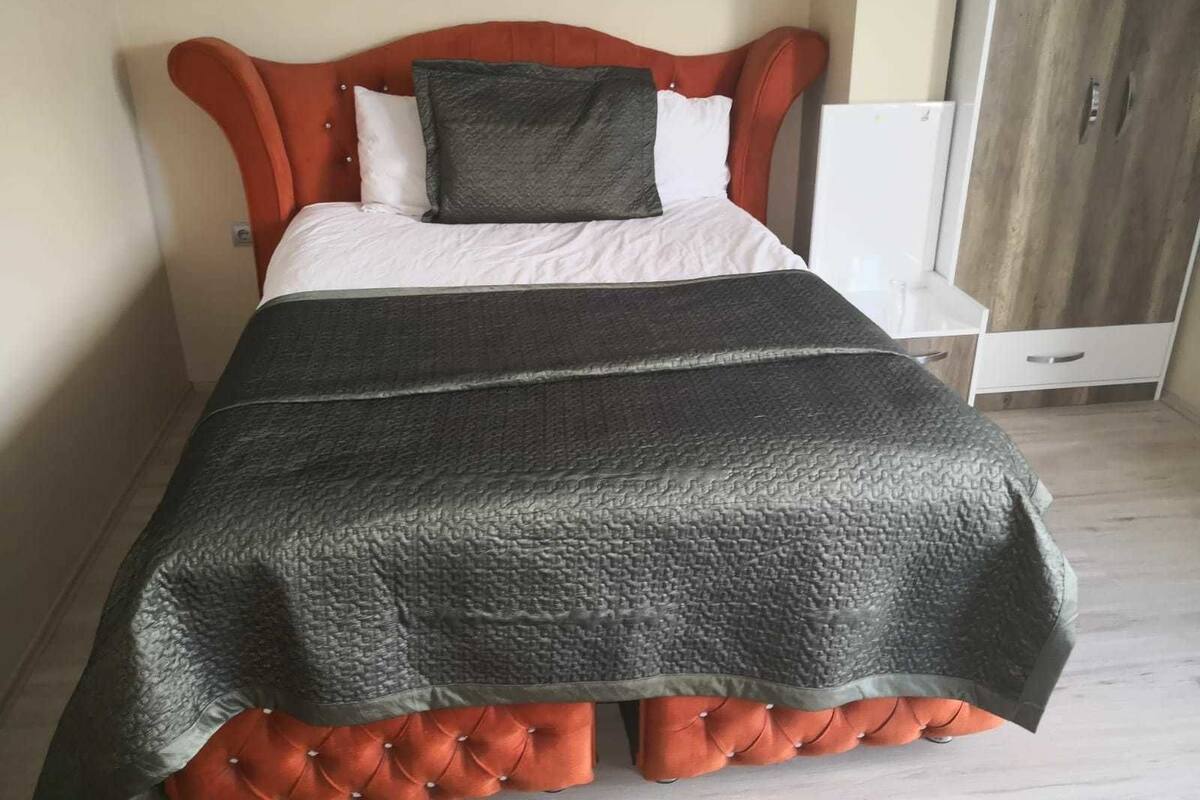 Un lit avec une tête de lit capitonnée, une couverture gris foncé et un oreiller blanc.