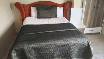 A bed with a tufted headboard, a dark grey blanket, and a white pillow.