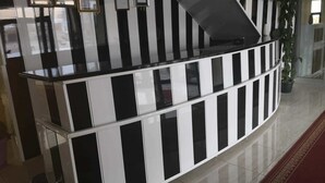 Un mostrador de recepción con diseño a rayas negras y blancas, certificados enmarcados en la pared y una planta en maceta a la derecha.