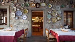 A restaurant with stone walls adorned with colorful plates, wooden tables with red tablecloths, and wicker baskets. - Agriturismo I Comelli (Nimis)