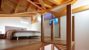 A modern loft bedroom with exposed wooden beams, a loft bed, a sofa, and a television. - Agriturismo I Comelli (Nimis)