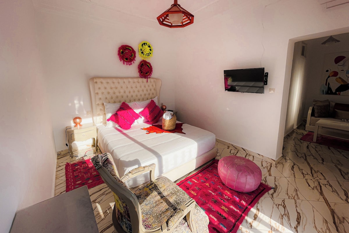 A bedroom with a bed, a TV, a red hanging decoration, and a patterned rug.