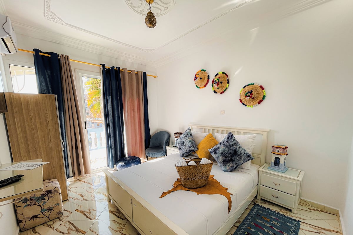 A bedroom with a bed, bedside table, chair, and a view of the outside.