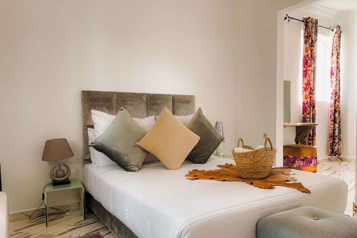 A bed with a wooden headboard, a bedside lamp, a woven basket, and a patterned rug.