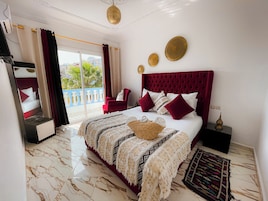 Una habitación de hotel con cama, una silla roja, un ventanal grande y un balcón.