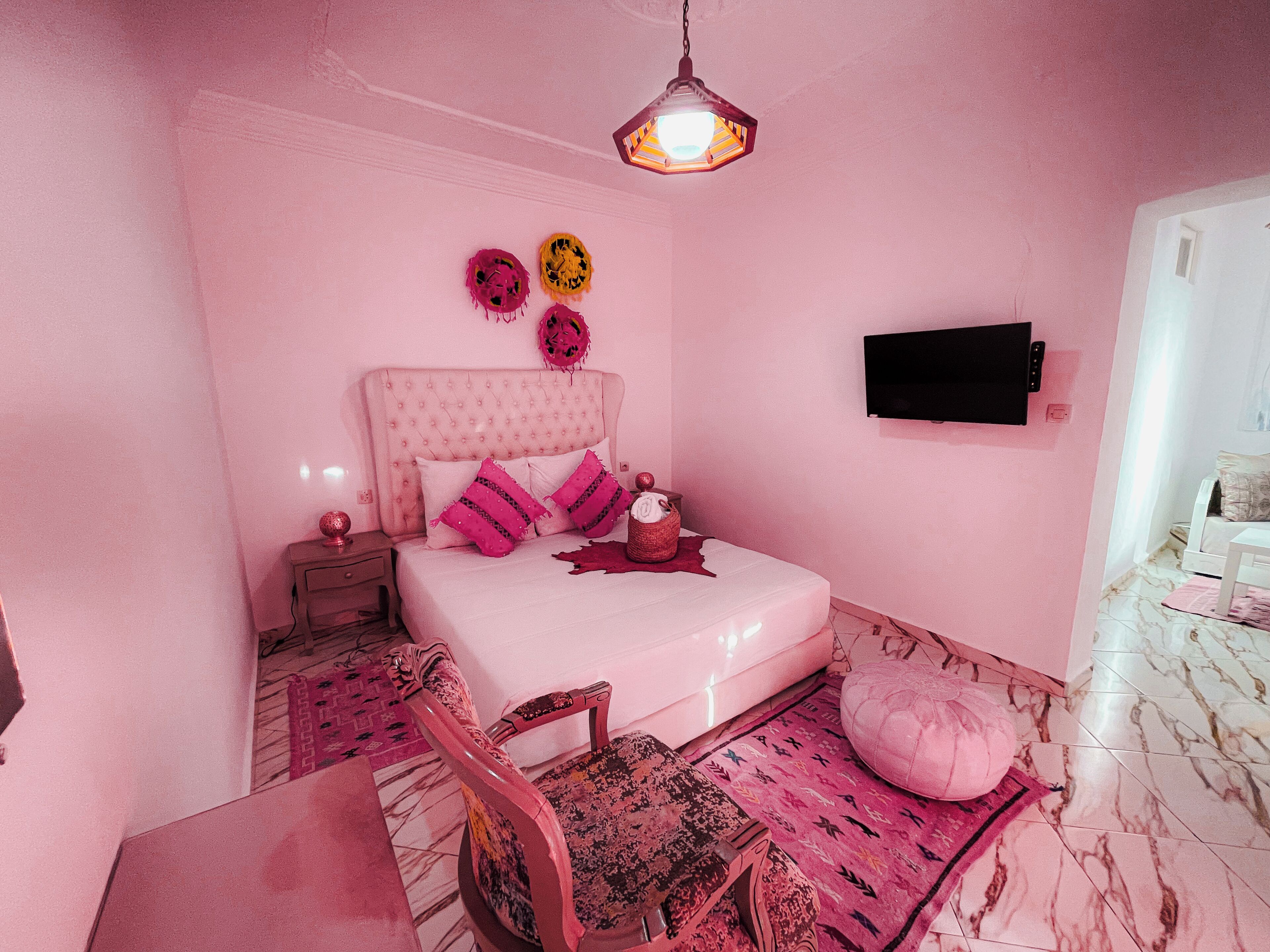 A pink-themed bedroom with a bed, a TV, a chair, and a rug.