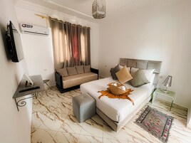 Una habitación de hotel con cama, sofá, televisión, lámpara y alfombra decorativa.