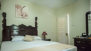A bedroom with a wooden bed, a nightstand with a lamp, a dresser, and a door.