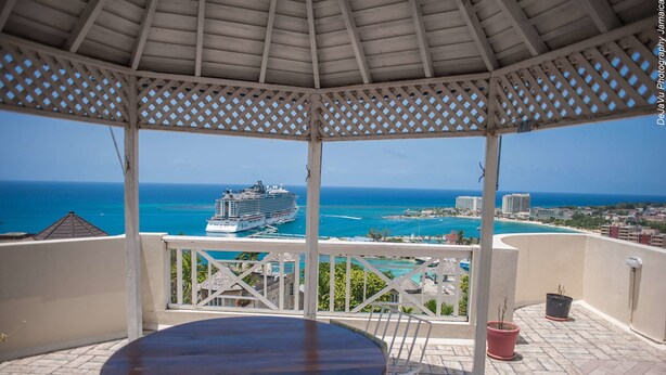 A covered outdoor area with a view of the ocean and a cruise ship.