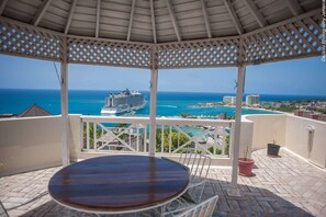 A covered outdoor area with a view of the ocean and a cruise ship.