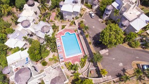 An aerial view of a resort with a central swimming pool, multiple villas, and a parking area.