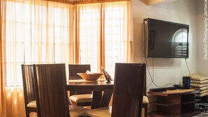 A dining area with a table, chairs, a television, and a window with curtains.