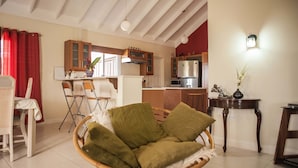 Una sala de estar acogedora con una silla de mimbre, un comedor con mesa y sillas, una cocina con electrodomésticos modernos y una pared de acento roja.