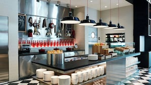 A modern kitchen with a checkered floor, stainless steel appliances, and a variety of utensils and cookware displayed on the wall. - citizenM Seattle South Lake Union (Seattle)