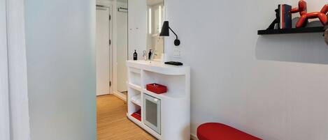 A modern bathroom with a white vanity, a red bench, and a large mirror.