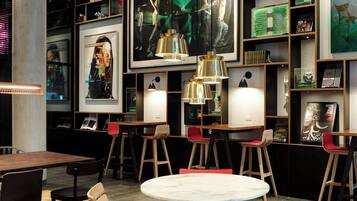A modern interior with a round dining table, red and black chairs, and a wooden floor. Shelves with books and decorative items line the walls.