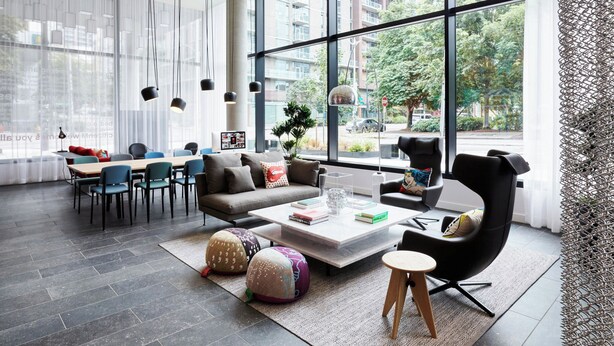 A modern living room with a large window, a sofa, a coffee table, and a dining area with chairs and a table. - citizenM Seattle South Lake Union (Seattle)