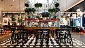 A modern bar area with checkered flooring, multiple seating options, and hanging plants. - citizenM Seattle South Lake Union (Seattle)