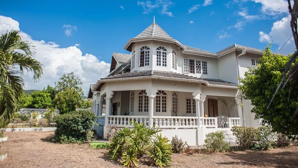 A large, two-story house with a balcony and a porch, surrounded by greenery. - Jewel In The Sand (Runaway Bay)