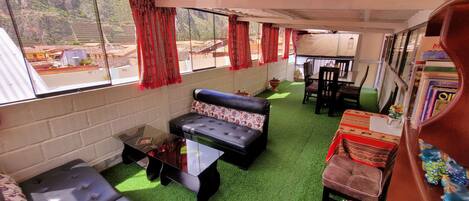 A room with a green artificial turf floor, a sofa, a glass coffee table, and a dining table with chairs.