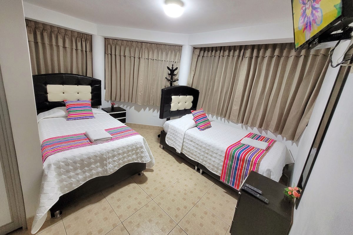 A hotel room with two beds, beige curtains, a ceiling light, and a TV on the wall.