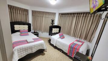 Una habitación de hotel con dos camas, cortinas color beige, una lámpara en el techo y un televisor en la pared.